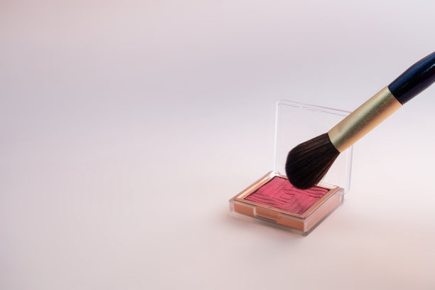 用金色的化妆刷在粉红色的背景上蘸上腮红图片下载