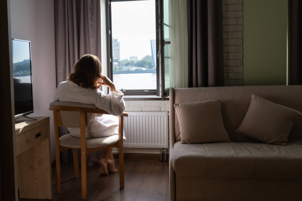 后视图的美丽的年轻女子在浴衣坐在扶手椅上，享受近开放的窗户在阳光明媚的早晨。图片下载