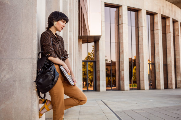 短发的年轻女子的侧视图，笔记本电脑和背包靠在墙上图片下载