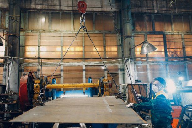 在工业工厂工厂，工人用带有遥控器和挂钩的吊车链葫芦吊起金属板。图片下载