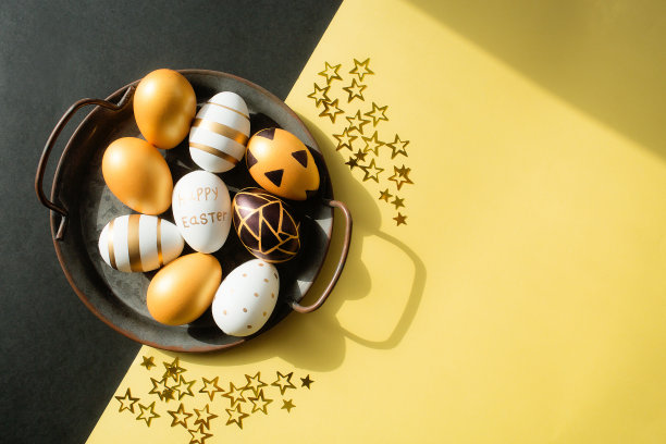 金色、黑色、白色的复活节彩蛋和黄黑色背景上星星形状的五彩纸屑。几何学。最小的概念。从以上观点。带有文本复制空间的卡片。图片下载