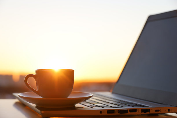 把咖啡或茶杯放在笔记本电脑上，靠在阳光下的窗户上图片下载