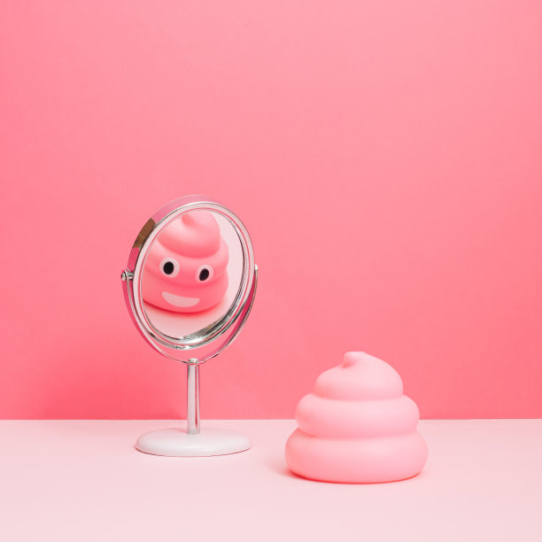 粉色便便表情符号看着镜子里的自己被孤立在淡粉色的背景下。有趣的概念。图片下载