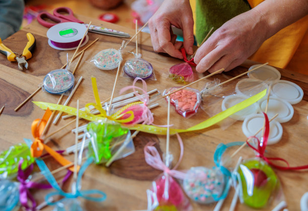 一名妇女在家庭糖果作坊的糖果店里为彩色棒棒糖系上丝带图片下载