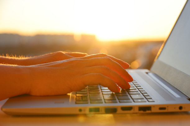 女性的手放在笔记本电脑键盘上，靠近阳光的窗户图片下载