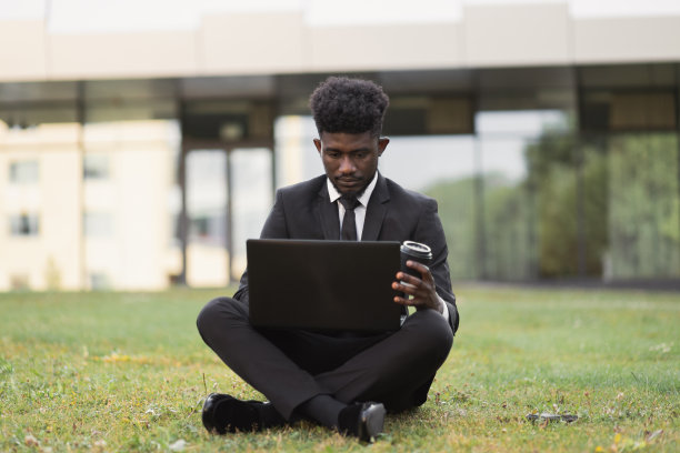 一名非洲裔美国人在户外使用笔记本电脑，坐在办公室附近的草地上图片下载