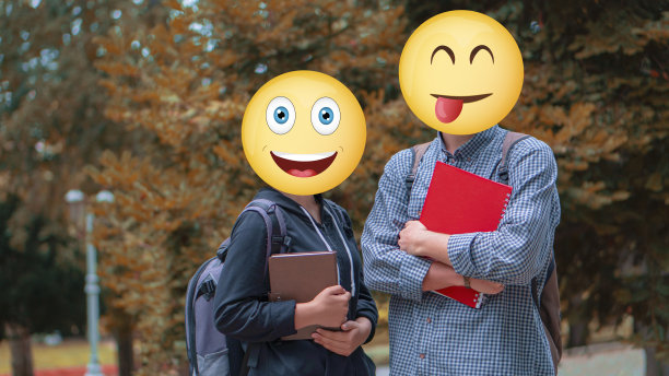 两个年轻的学生拿着笔记本在外面摆姿势。他们无法辨认，因为他们脸上有表情符号。目前还不清楚他们是谁。背景表明现在是秋天。叶子变黄的树出现了。图片下载