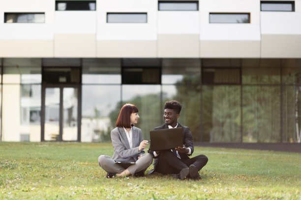 多种族的男女同事坐在办公室外的草地上用笔记本电脑工作图片下载