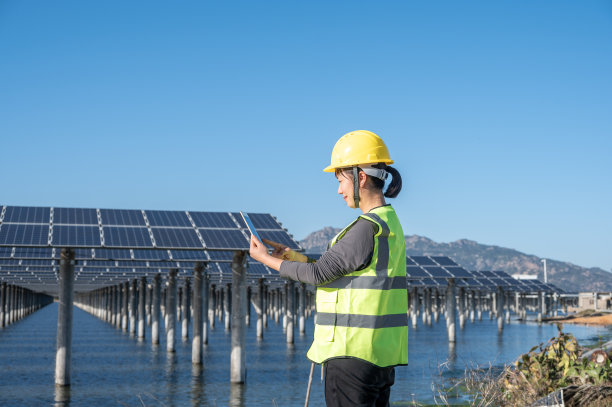在蓝天下，一位亚洲妇女在海边的光伏太阳能电站用平板电脑工作图片下载