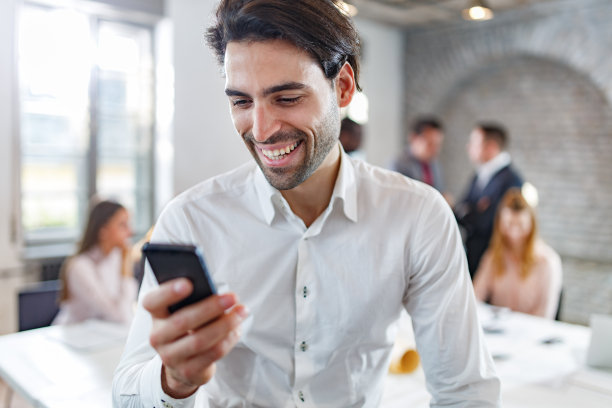 年轻快乐的商人在办公室使用智能手机。图片下载