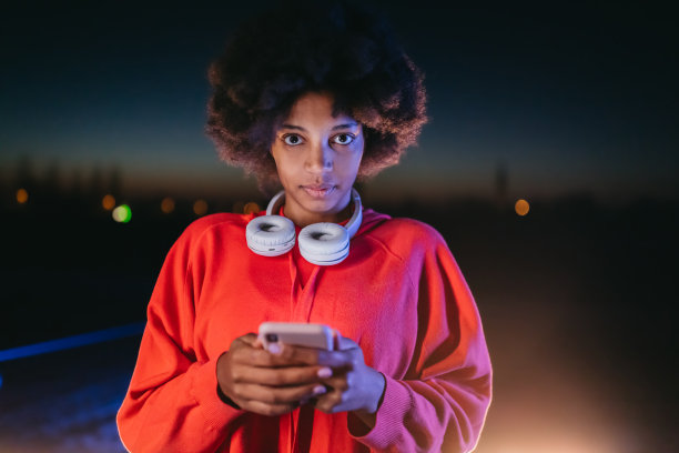非洲年轻女子戴着耳机在晚上使用手机图片下载