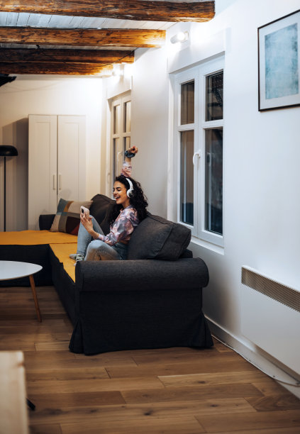 年轻女子坐在房间的沙发上，戴着耳机听音乐图片下载