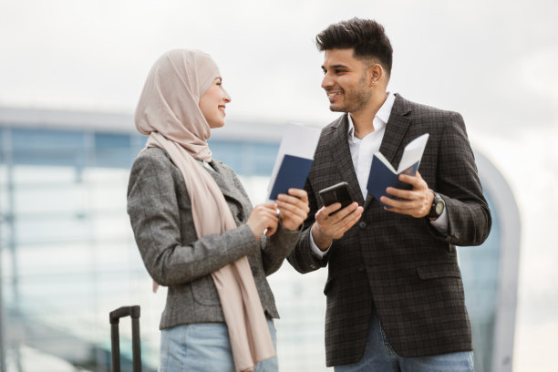 阿拉伯夫妇，拿着行李站在机场候机楼外，检查他们的登机牌图片下载