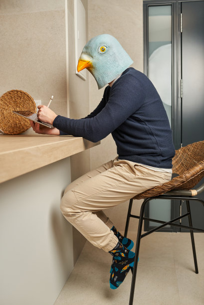 一名男子伪装成一只鸟的面具，在他的数码平板电脑上作画图片下载