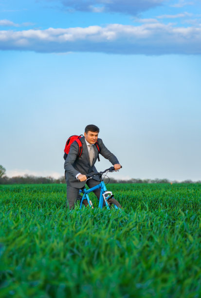 一个商人背着背包骑着自行车穿过绿油油的草地，穿着西装，美丽的大自然春天，经营理念图片下载