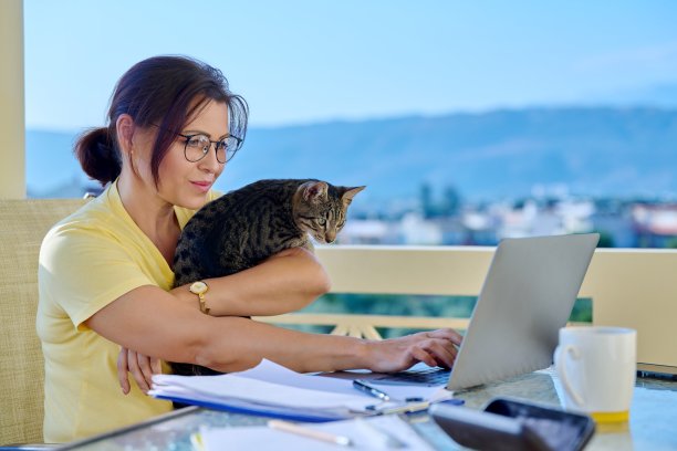 在家工作的女性自由职业者远程工作与宠物猫在她的手臂图片下载