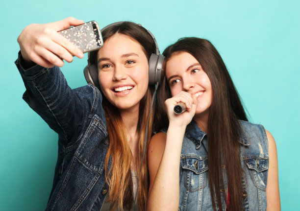 年轻的美女们拿着麦克风唱歌，用智能手机拍照图片下载