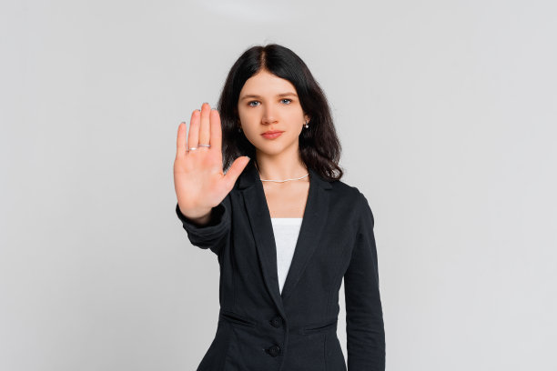 求你了，不要，停下。年轻严肃的黑发女孩，站在灰色的背景上，看着镜头，伸出手臂示意停车。呆在家里。社会距离。新常态行为图片下载