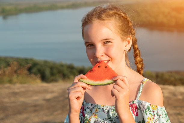 小女孩扎着辫子，在河边咬着多汁的西瓜图片下载