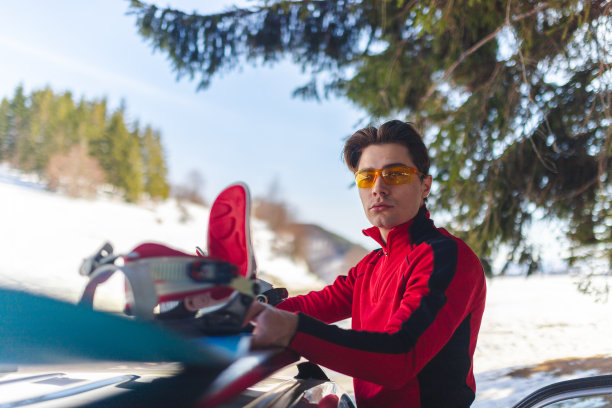 一个英俊的年轻人在树林里把滑雪板从车顶上拿下来图片下载