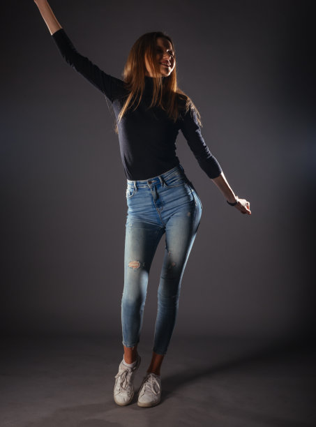 迷人的女模特在牛仔布牛仔裤摆孤立的灰色背景。图片下载