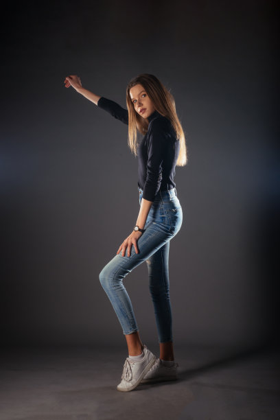 一名年轻女模特的侧面全身肖像，穿着黑色上衣和牛仔裤，一条腿在前面摆姿势图片下载