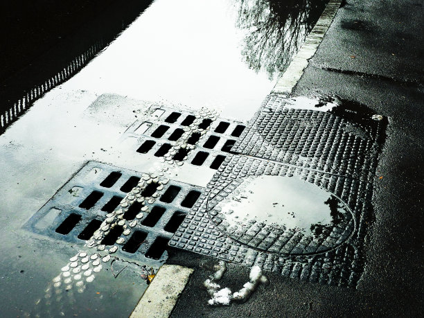 流入下水道沙井的水。路面潮湿，有下水道。图片下载