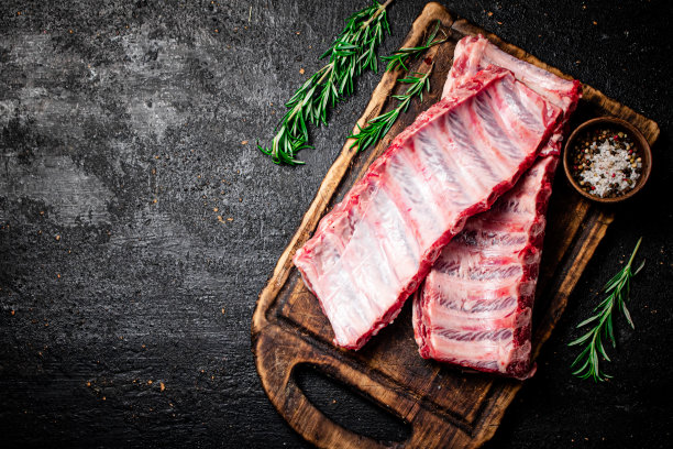 在切菜板上放着迷迭香和香料的生排骨。图片下载