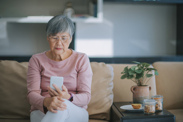 亚洲华人老年妇女使用智能手机阅读短信在她的公寓在城市图片下载
