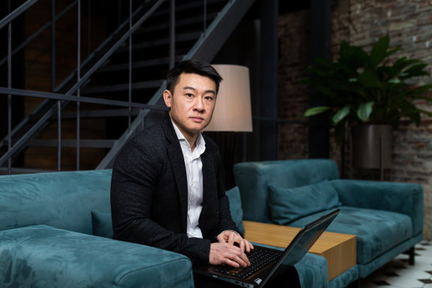 成功的亚洲商人，穿着黑色西装，在笔记本电脑上工作，在餐厅或酒店休息，在一个时尚的办公室通过视频链接解释一个新的商业战略图片下载