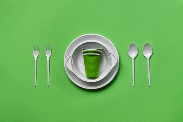 彩色塑料一次性餐具在绿色背景与复制空间。野餐用具的概念。前视图。有选择性的重点。特写镜头图片下载