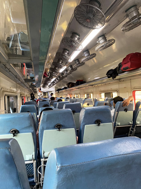 印度火车车厢内部的特写图像，头顶上的风扇，头顶上打开的行李架，折叠桌子的座位图片下载