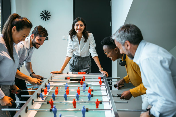 在现代化的办公室里，面带微笑、来自不同民族的同事们在玩桌上足球图片下载
