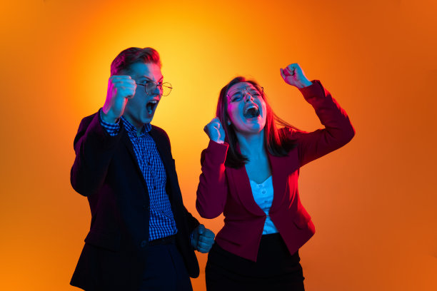 这是一幅年轻男女的肖像，他们戴着眼镜，穿着夹克，在霓虹灯下的橙色工作室背景下，表情激动图片下载