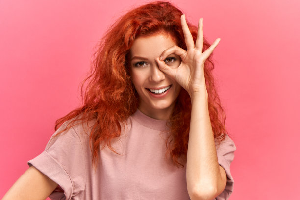 有趣的红发女少年穿着休闲t恤，有快乐的表情，闭上她的一只眼睛，愉快地有广泛的微笑，在粉红色的背景上嬉戏图片下载