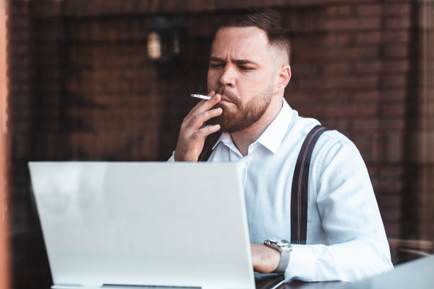 一个年轻的商人在咖啡馆里用笔记本电脑工作，抽烟图片下载