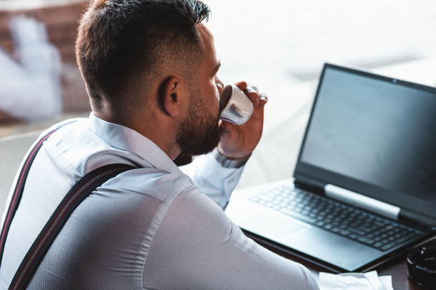 一个年轻的商人在咖啡馆里用笔记本电脑工作，喝着浓咖啡图片下载