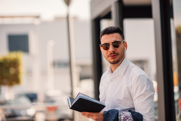 一个雄辩的商人在外面，他一边享受着美好的天气，一边看着笔记本。城市商人的迁徙。图片下载