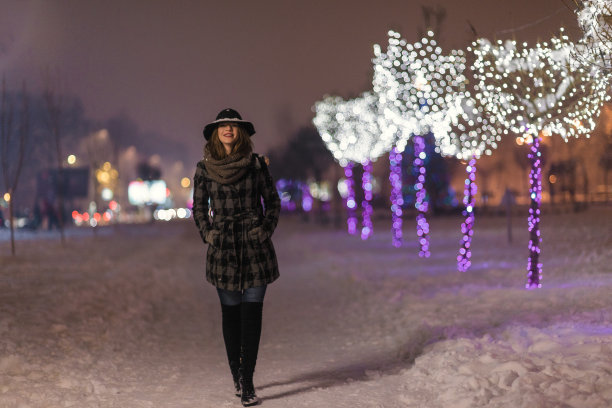 年轻的女孩走在装饰着彩灯的圣诞树前，在圣诞节的夜晚，模糊在背景中图片下载