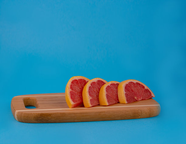 葡萄柚切成片。葡萄柚躺在蓝色背板的木板上。红葡萄柚。图片下载
