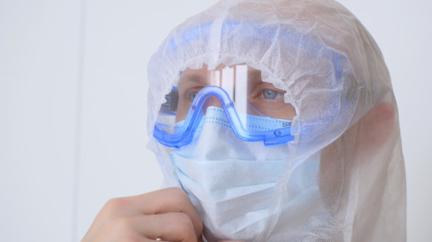 一位疲惫的男医生在下班后，脱下长袍的兜帽、面罩和护目镜。一名卫生工作者对感染冠状病毒的患者的工作。新型传染病图片下载