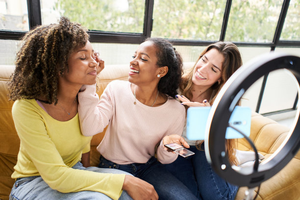 美妆博主在三脚架上拍摄日常化妆教程。非洲女孩影响者在家庭工作室直播化妆品产品评论。女视频博主为她的朋友化妆图片下载