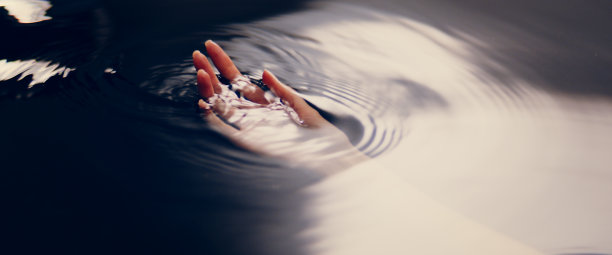 纤细的女性之手从黑暗的水中浮现。带光束的圆波。自然美容护理的隐喻。图片下载