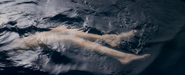 一个女人漂浮在黑暗的水面上。贴近腿与光滑的皮肤。美容护理的比喻图片下载