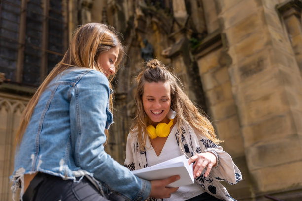两个年轻的白人妇女坐在教堂旁看书图片下载