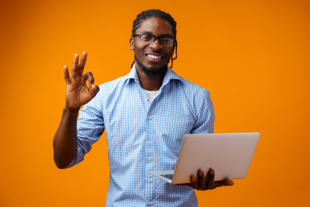 年轻的非洲男子微笑着站在黄色背景上使用笔记本电脑图片下载