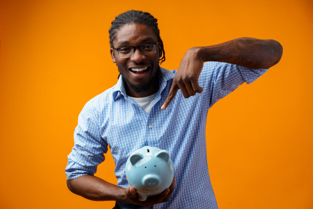 年轻的非裔美国黑人拿着一个储蓄罐，背景是橙色的。图片下载