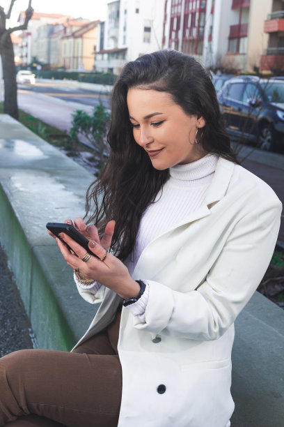 一名年轻的白人女子坐在海滨长廊的长椅上使用智能手机。图片下载