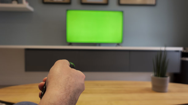 一名男子坐在沙发上，把电视频道的遥控器调到电视机的背景上图片下载