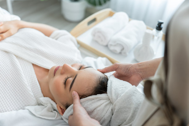 亚洲年轻女性在面部和头部按摩时感到快乐和放松。美丽迷人的女孩躺在按摩台上，在水疗美容院接受按摩师的皮肤和身体理疗。图片下载